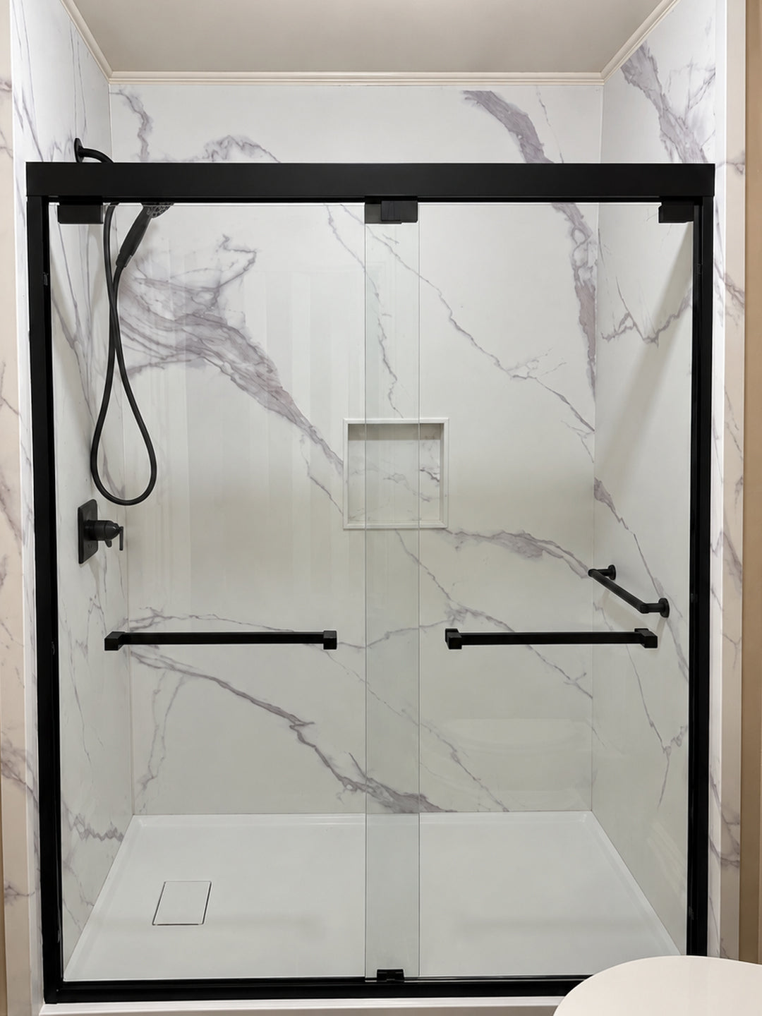 After: marble-look shower with black-framed glass doors and white base
